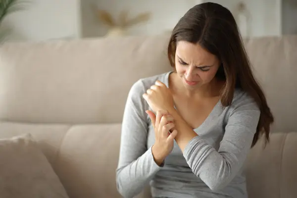 Młoda kobieta ze skrzywioną miną dotyka swoich rąk, gdyż dokucza jej świąd spowodowany szorstką skórą.